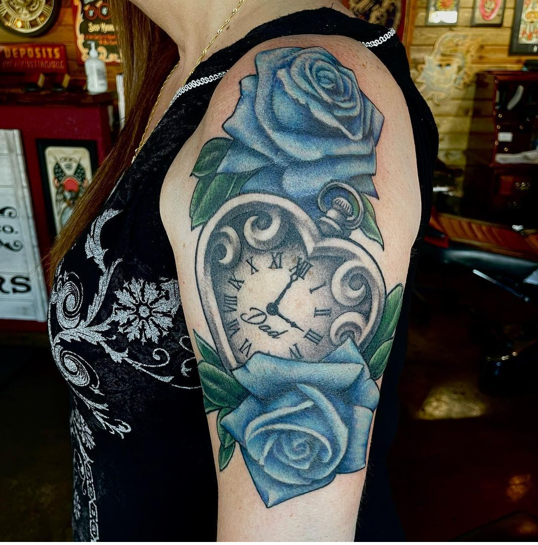 Tattoo of a clock and two blue roses from shop in Dallas Texas