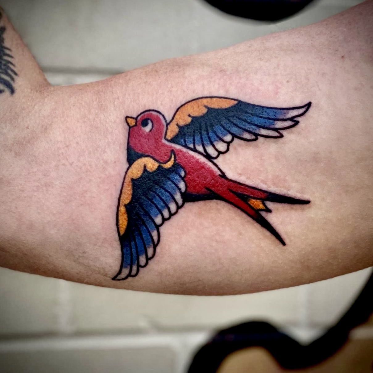 Tattoo of a red, yellow, and blue bird